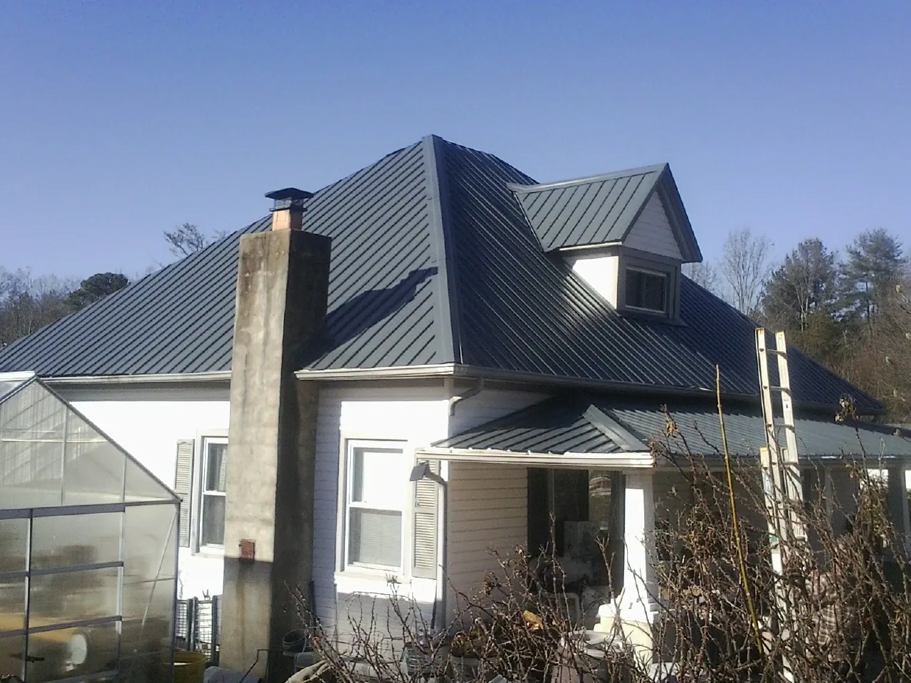 Dark blue standing seam metal roof on a white farmhouse with dormer — Slate & Tile Roof Repair by Roofing Brothers in Bensenville