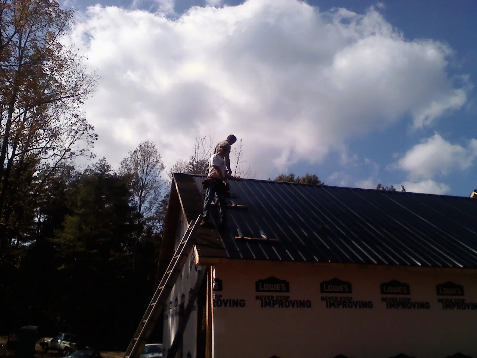 Roofer fastening dark metal panels high against a cloudy sky, from a Roof Inspection job in Bensenville