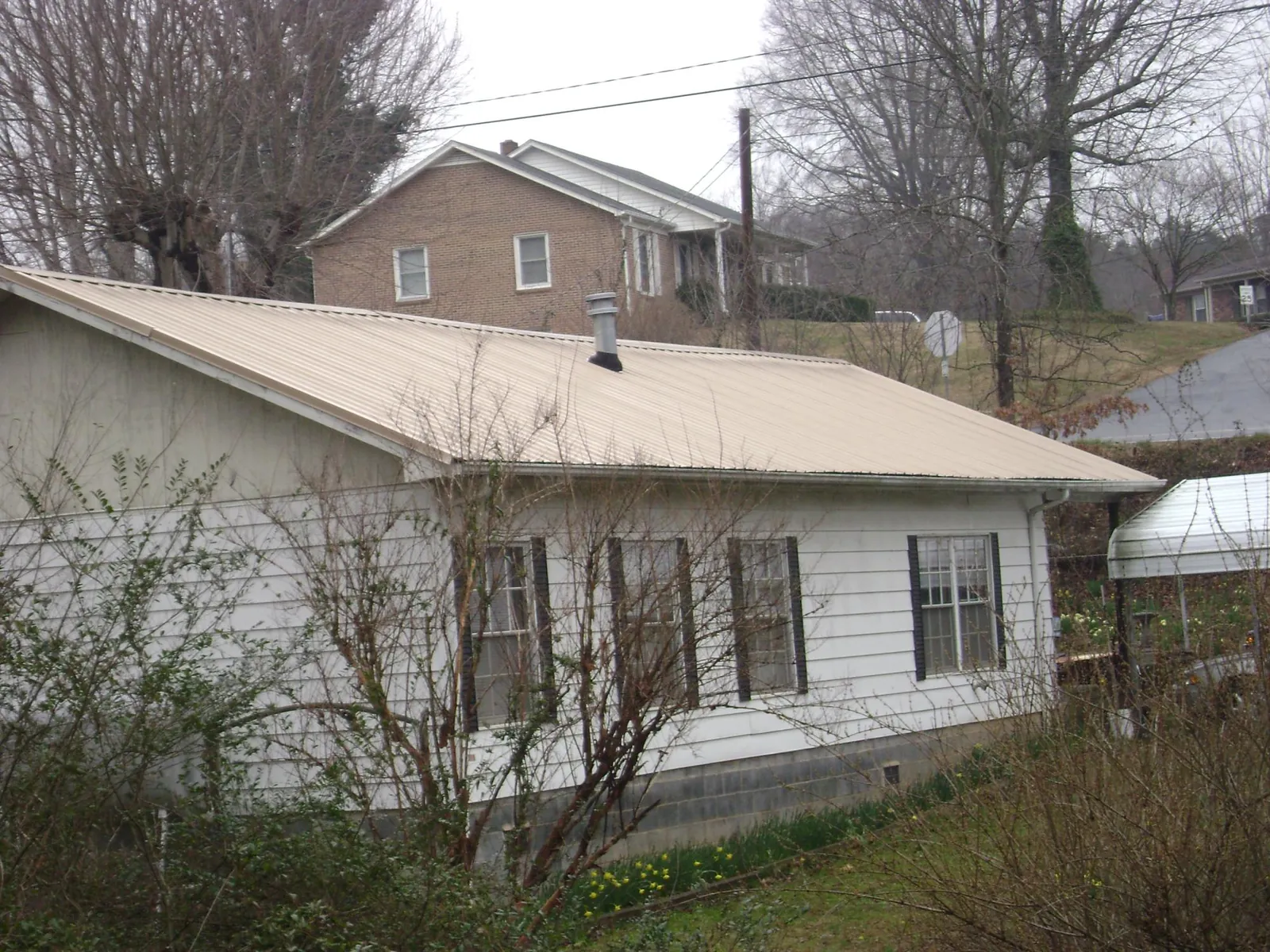 Tan metal roof on a white sided house set into a hillside — Commercial Roofing by Roofing Brothers in Bensenville